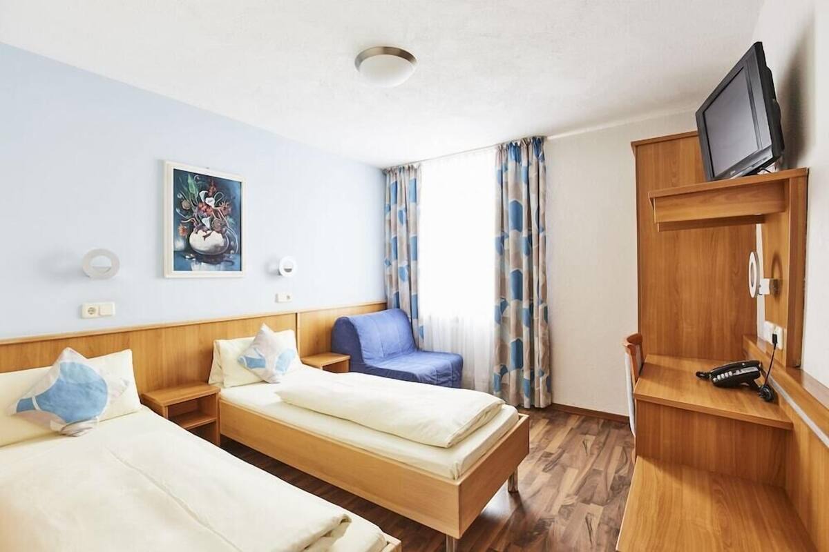 Et hotelværelse med to senge, et fjernsyn på en træhylde, en stol og et billede på væggen.