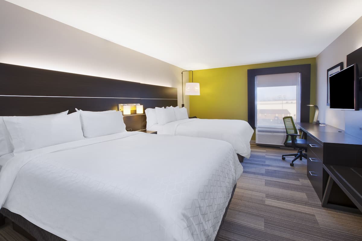 A hotel room with two beds, a desk, a chair, a TV, and a window with a view.