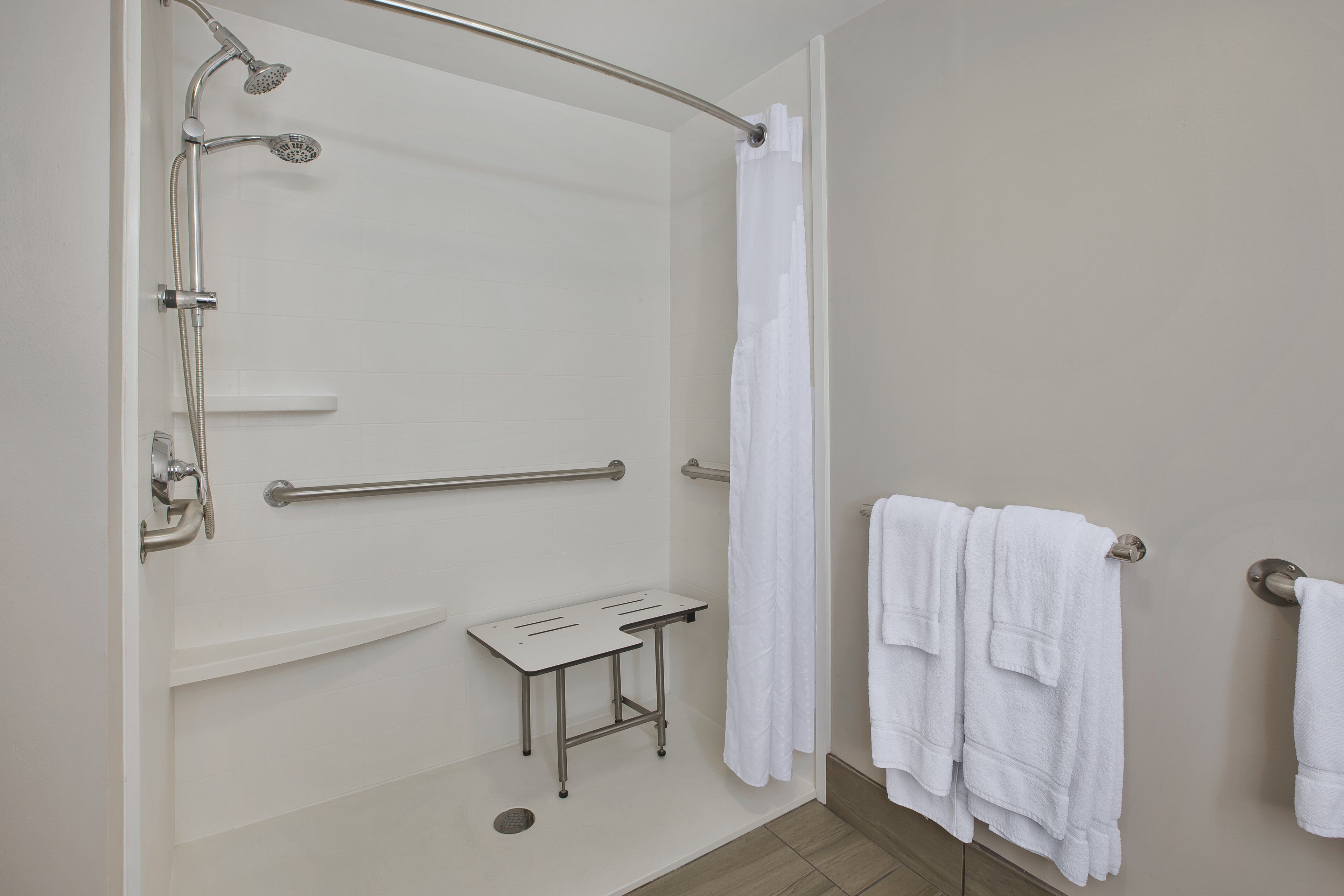 Un baño con ducha, barras de apoyo, una mesita y toallas.