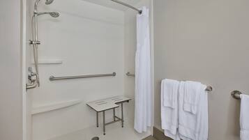 Un baño con ducha, barras de apoyo, una mesita y toallas.