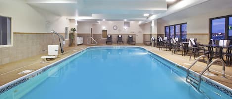 A swimming pool with a lounge area, chairs, and a clock on the wall.
