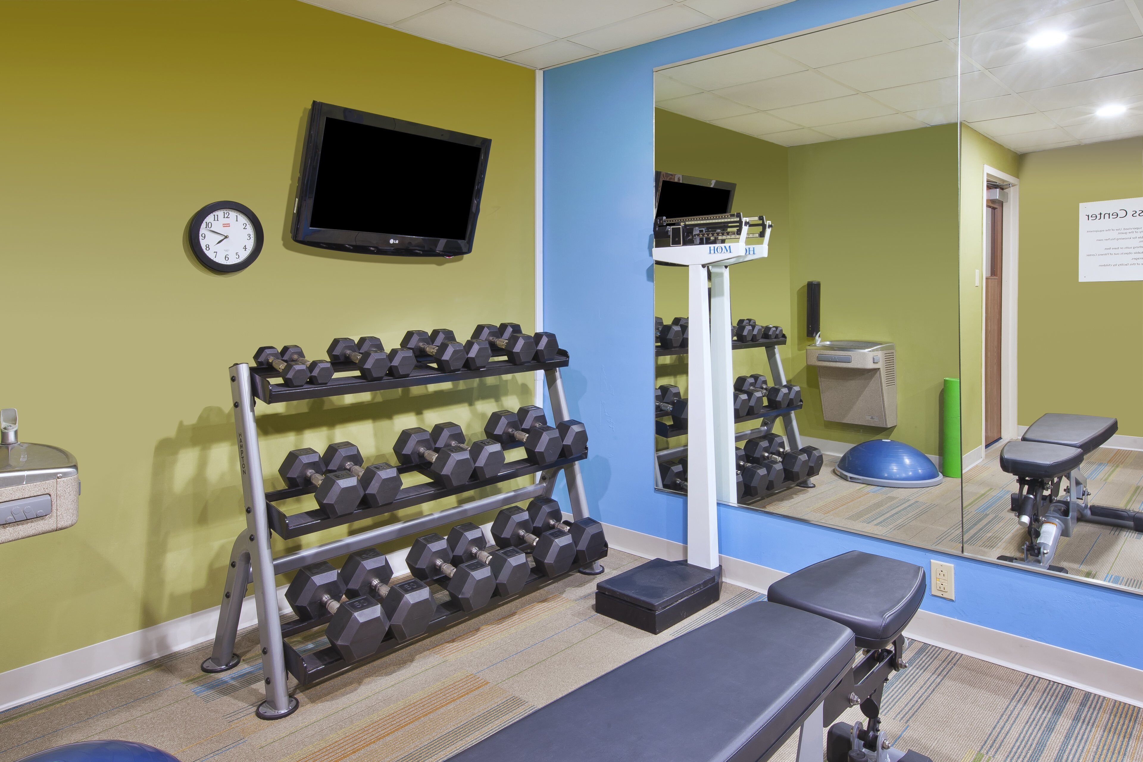 Une salle de sport équipée d’un banc, d’haltères, d’un tapis de course et d’un miroir.