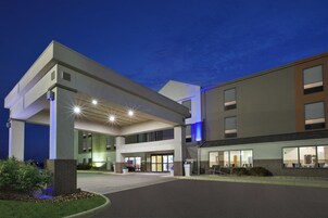 Entrada de hotel com área de estacionamento coberta, céu claro e fachada bem iluminada.