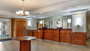 A modern hotel lobby with a round wooden reception desk, a chandelier, and a large mirror with a crescent moon design. - Comfort Inn & Suites Hadley - Amherst (Hadley)