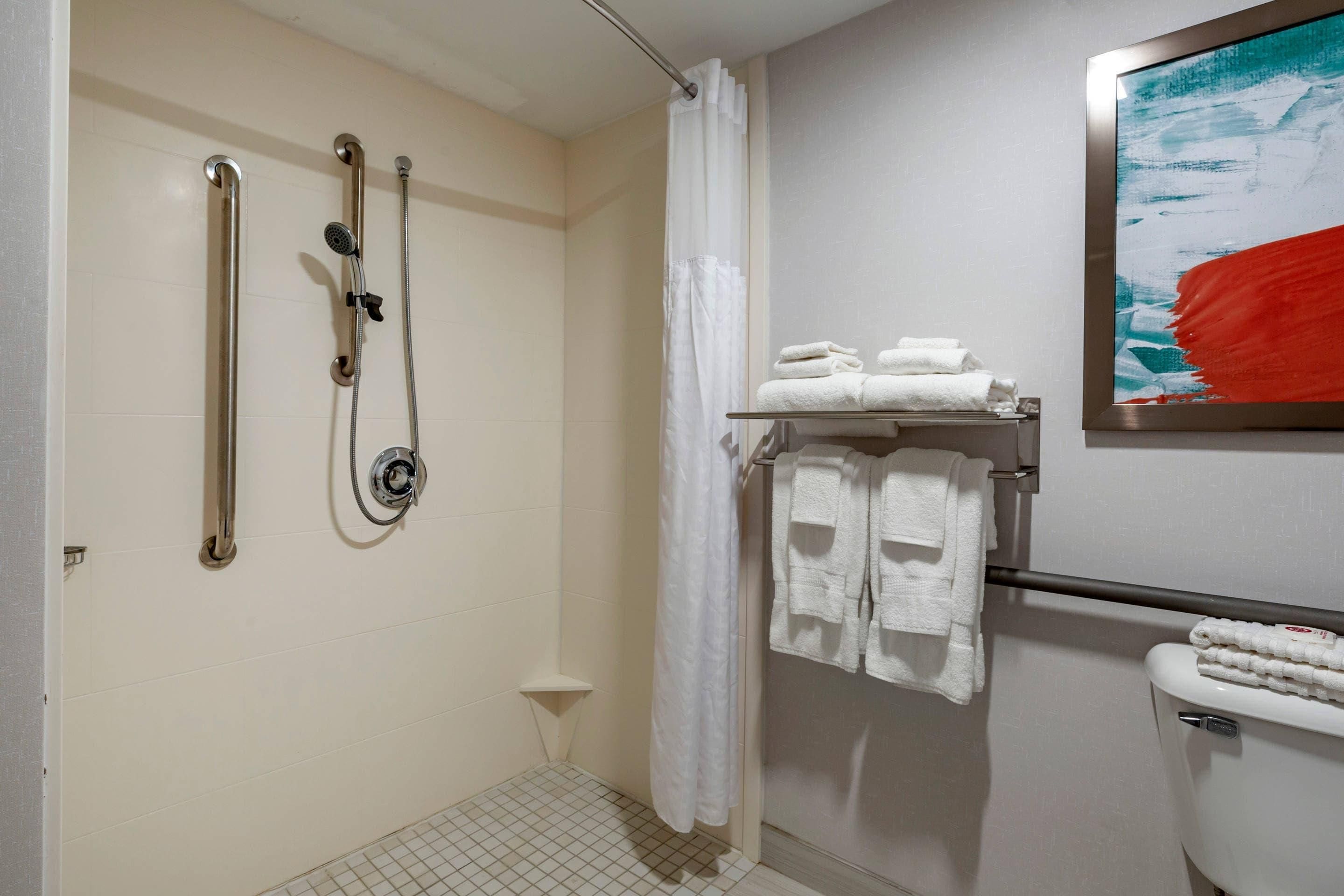 Une salle de bain équipée d’une douche, de barres d’appui, de toilettes et d’un porte-serviettes avec des serviettes pliées.