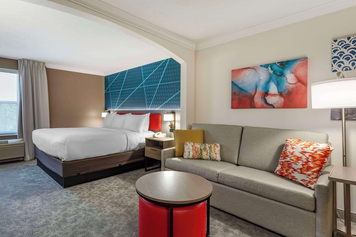 A hotel room with a bed, a sofa, a round coffee table, and a nightstand.