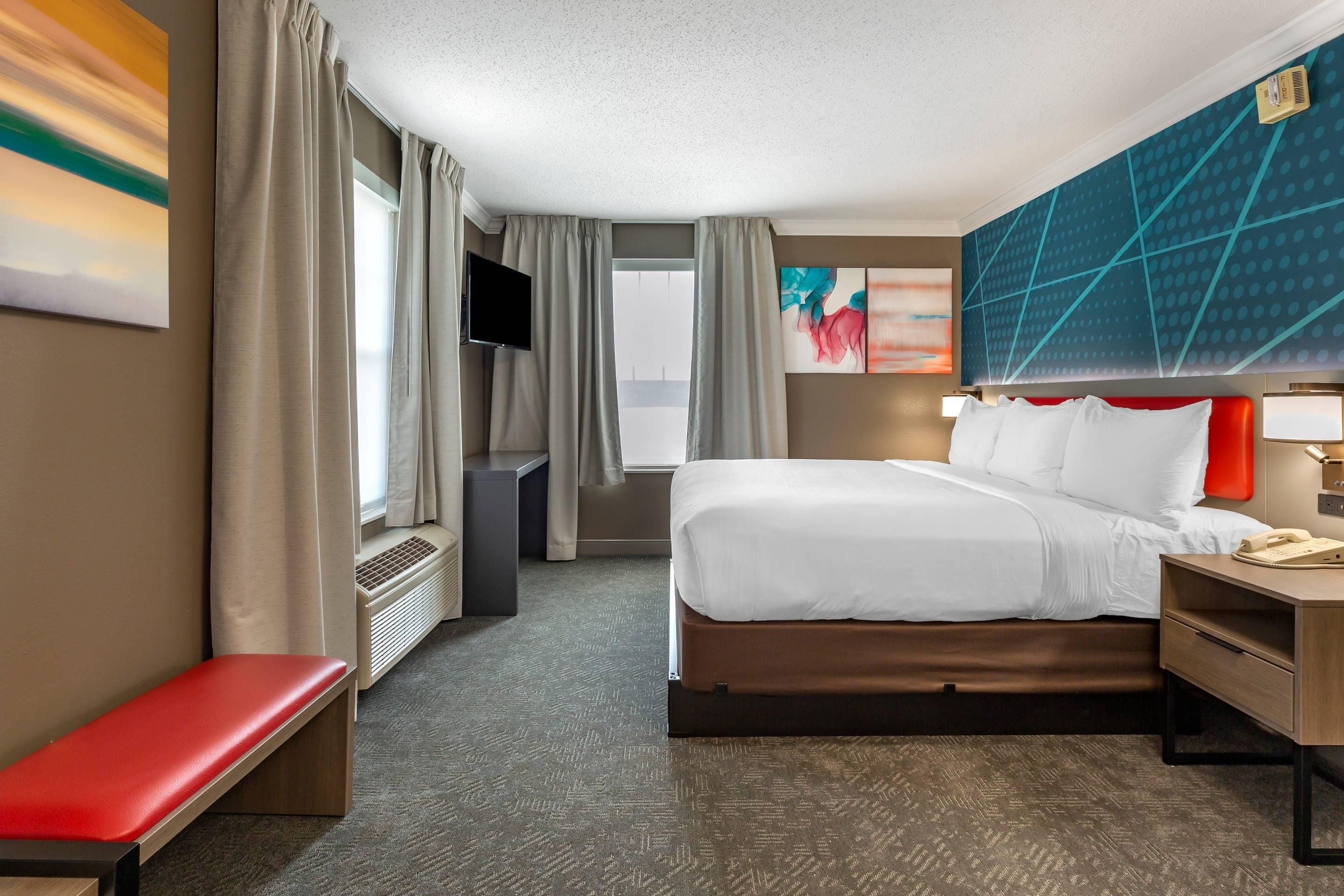 Een hotelkamer met een bed, nachtkastje, televisie en een bankje.