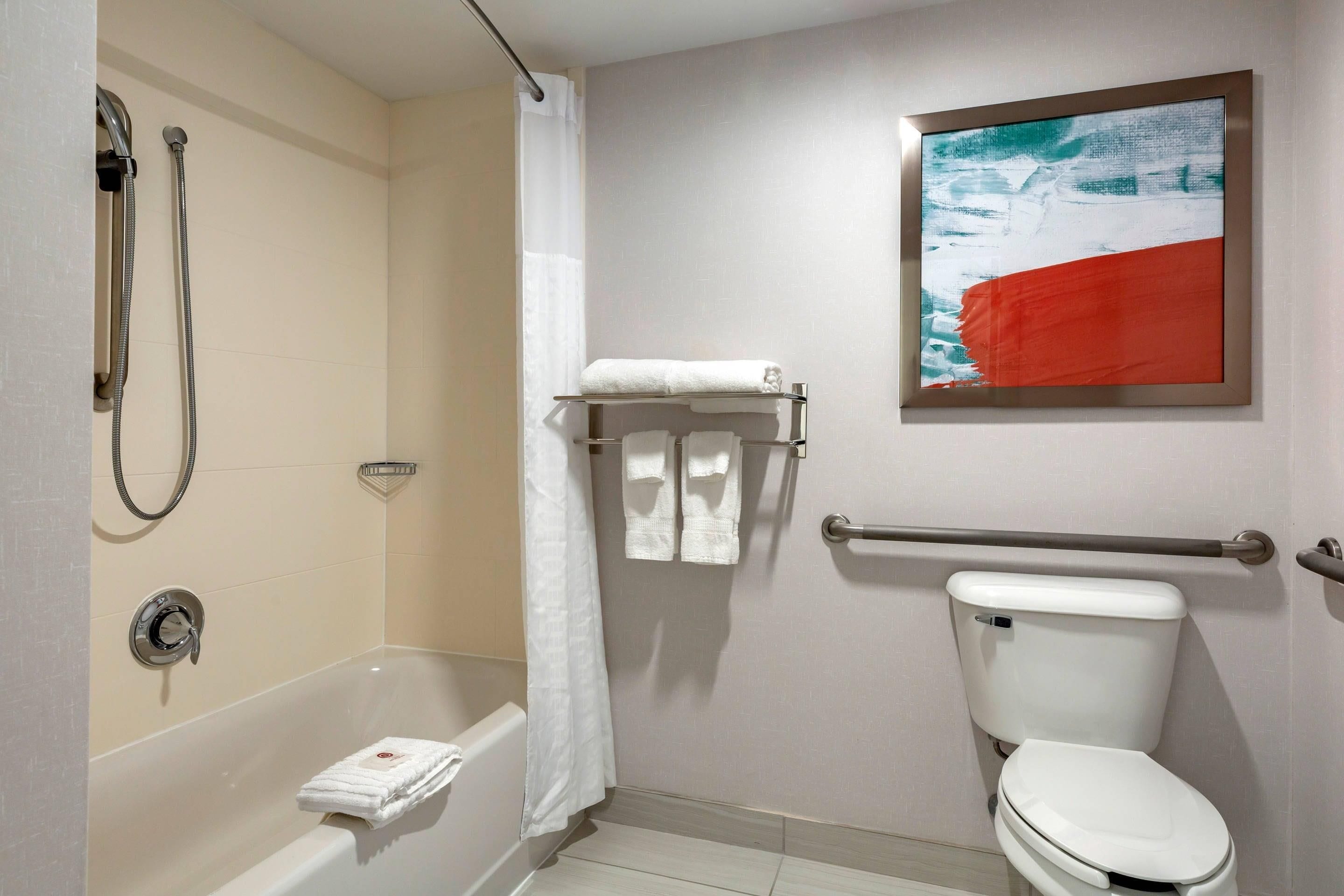Et badeværelse med badekar, toilet og bruser. Der er et håndklædetørrestativ med håndklæder og et billede i ramme på væggen.