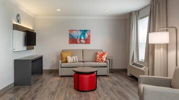 A modern living room with a sofa, a red ottoman, a flat-screen TV, and a painting on the wall.