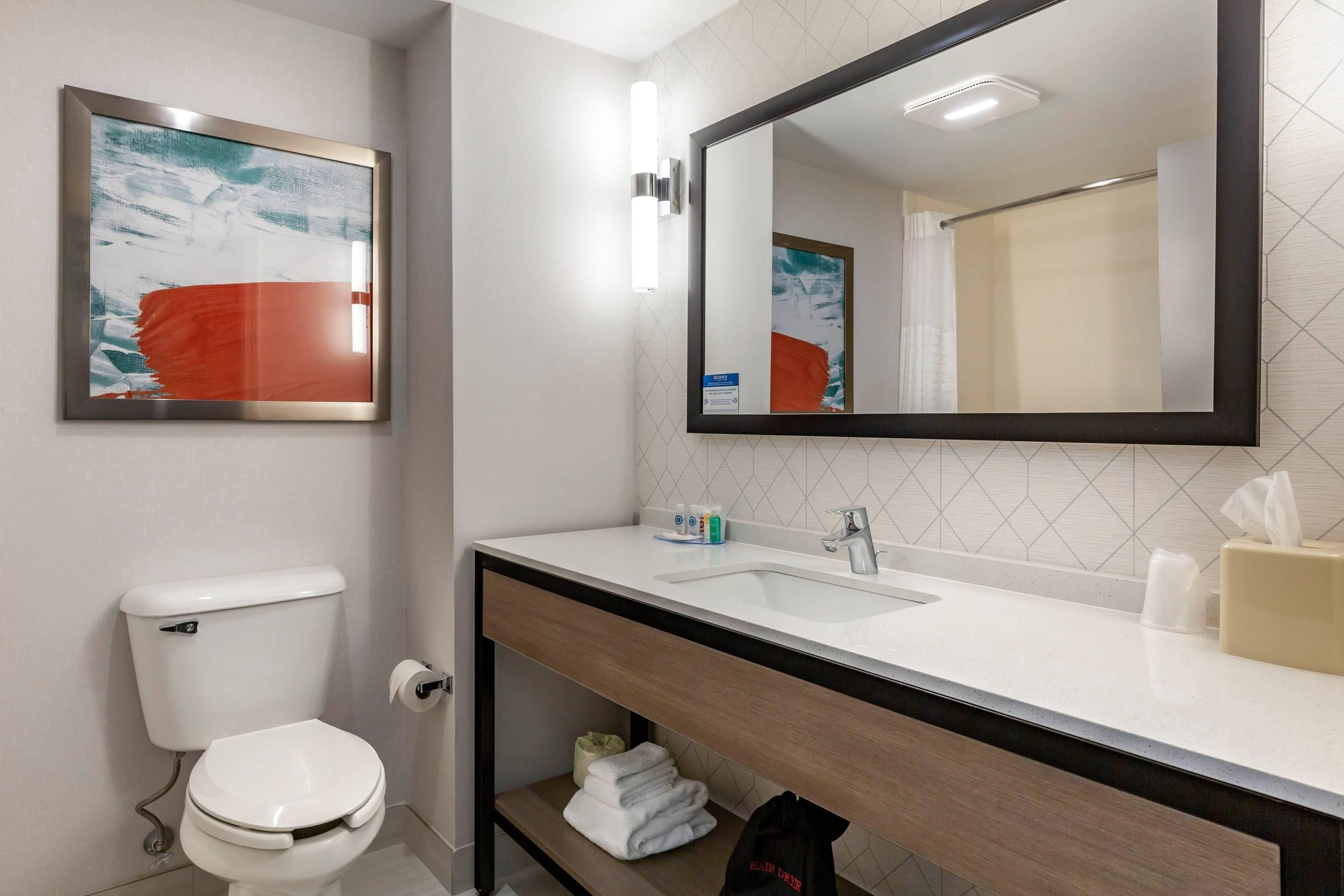A modern bathroom with a toilet, sink, mirror, and a towel rack.