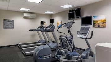 A fitness room with treadmills, an elliptical, and a stationary bike, equipped with digital displays and a wall-mounted TV.