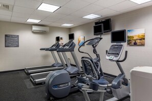 A fitness room with treadmills, an elliptical, and a stationary bike, equipped with digital displays and a wall-mounted TV.