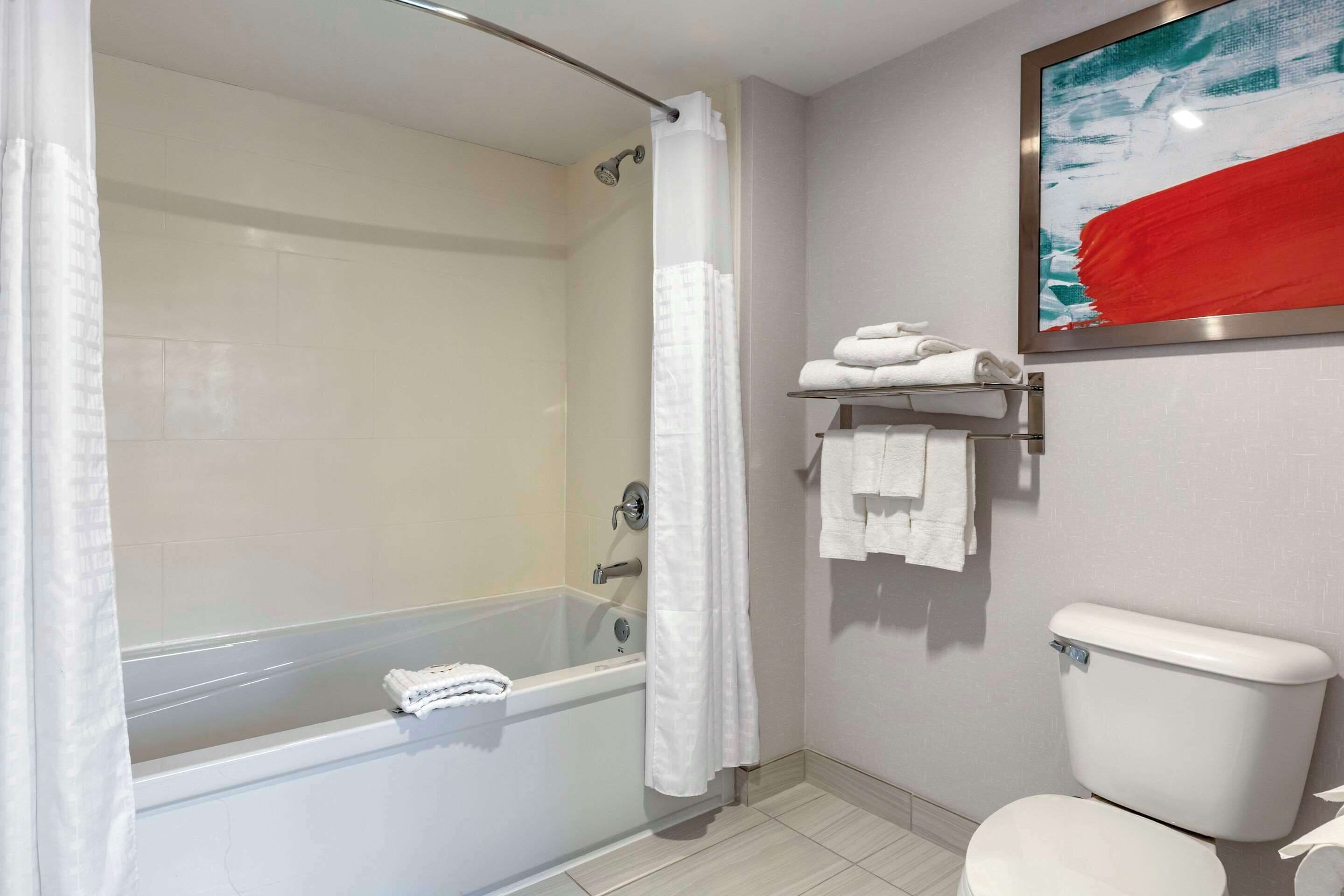 Un baño con bañera, ducha, inodoro y un perchero con toallas.