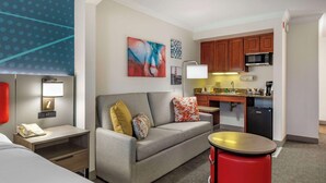 A hotel room with a sofa, a small table, a red stool, a kitchenette, and a bed. - Comfort Inn & Suites Hadley - Amherst (Hadley)