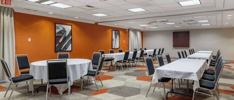 A conference room with multiple tables and chairs, an exit sign, and a patterned carpet.