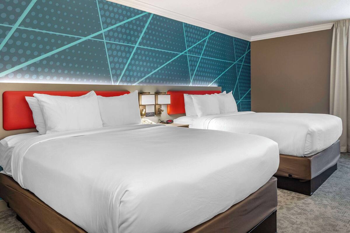 A hotel room with two beds, a modern wall design, and a neutral color scheme.