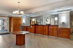 Een hotel lobby met een receptiebalie, een ronde tafel met een decoratief middelpunt, en een kroonluchter.