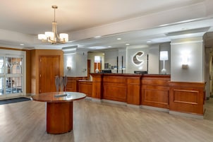 A hotel lobby with a reception desk, a round table with a decorative centerpiece, and a chandelier.