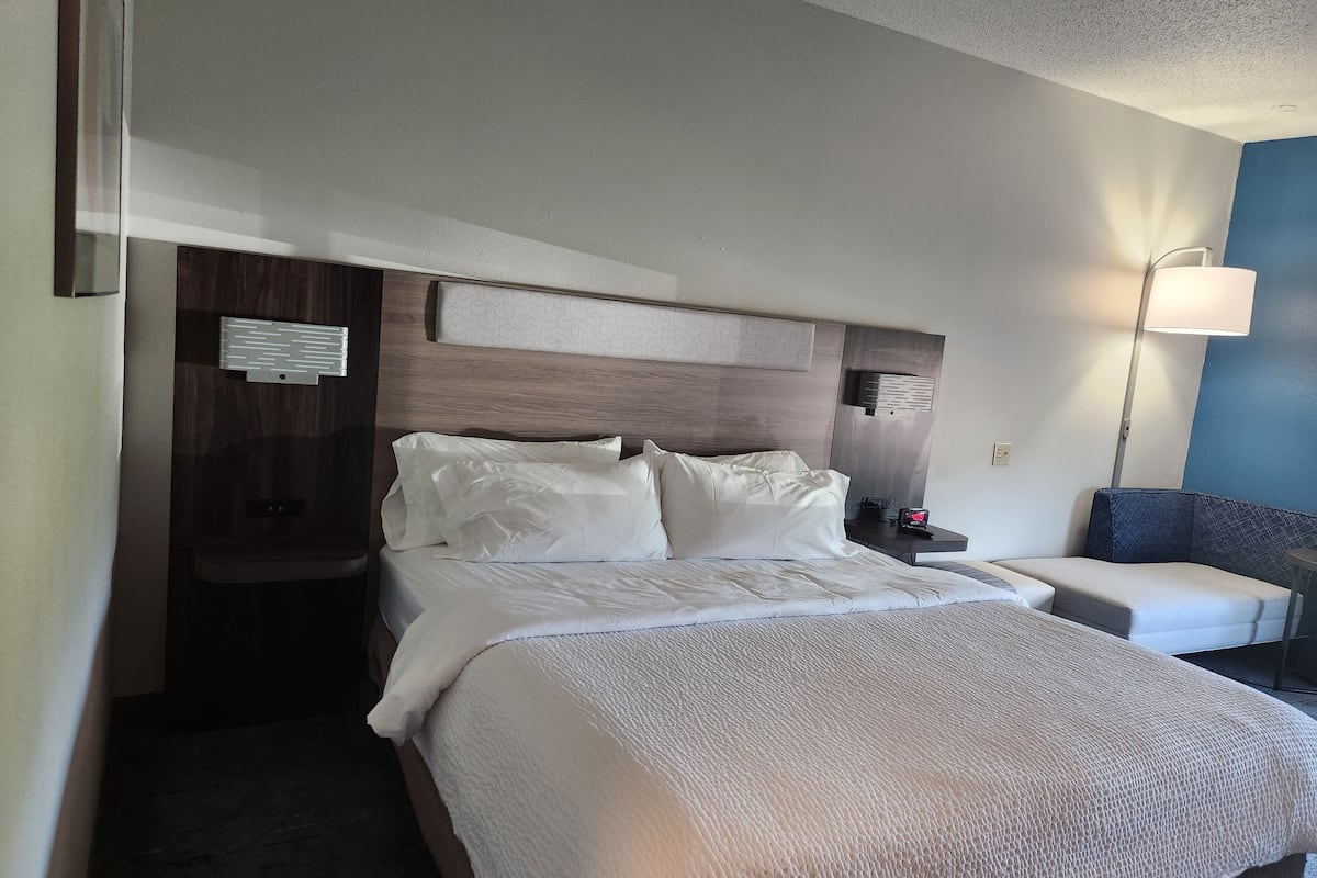 A hotel room with a large bed, a nightstand, a lamp, and a seating area.