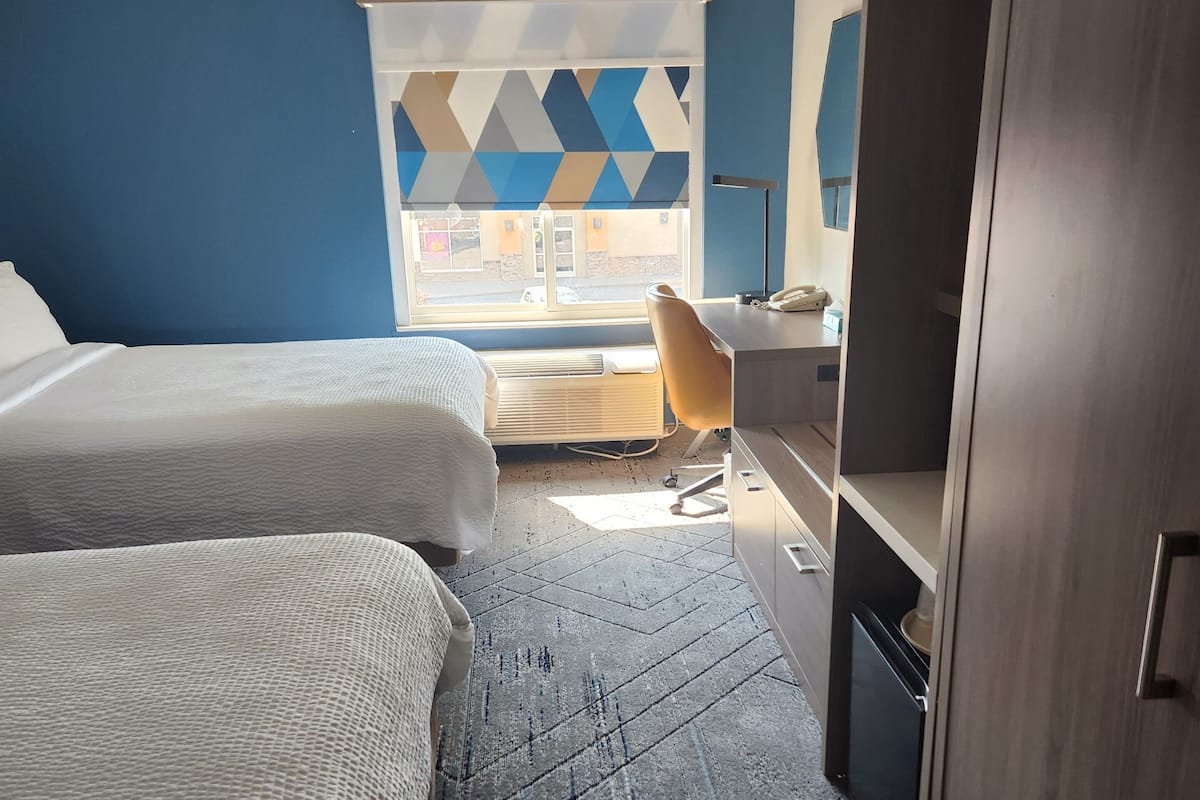 A hotel room with two beds, a desk, a chair, and a wardrobe.