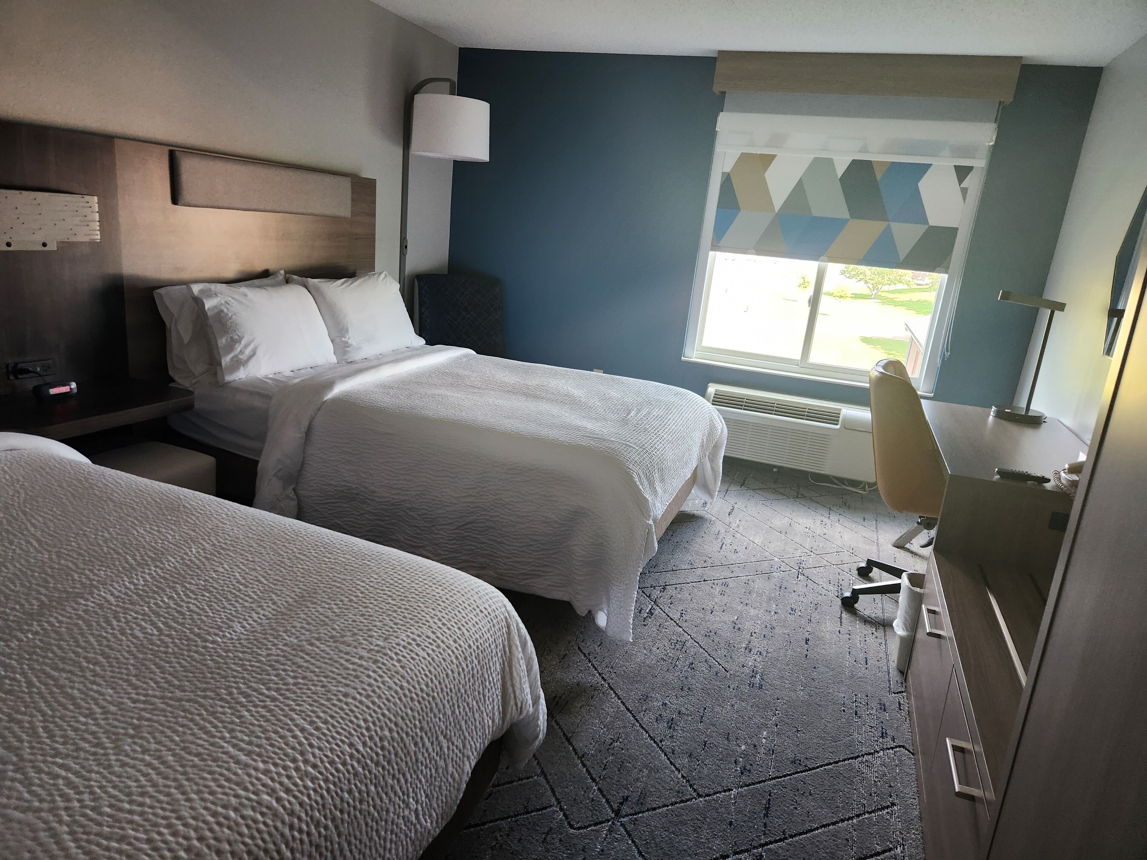A hotel room with two beds, a desk, a chair, and a window with a view of the outdoors.