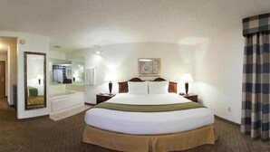 A hotel room with a large bed, a mirror, a bedside table with a lamp, a painting on the wall, and a view of the hallway. - Holiday Inn Express & Suites Alliance by IHG (Alliance)