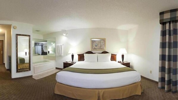 A hotel room with a large bed, a mirror, a bedside table with a lamp, a painting on the wall, and a view of the hallway. - Holiday Inn Express & Suites Alliance by IHG (Alliance)