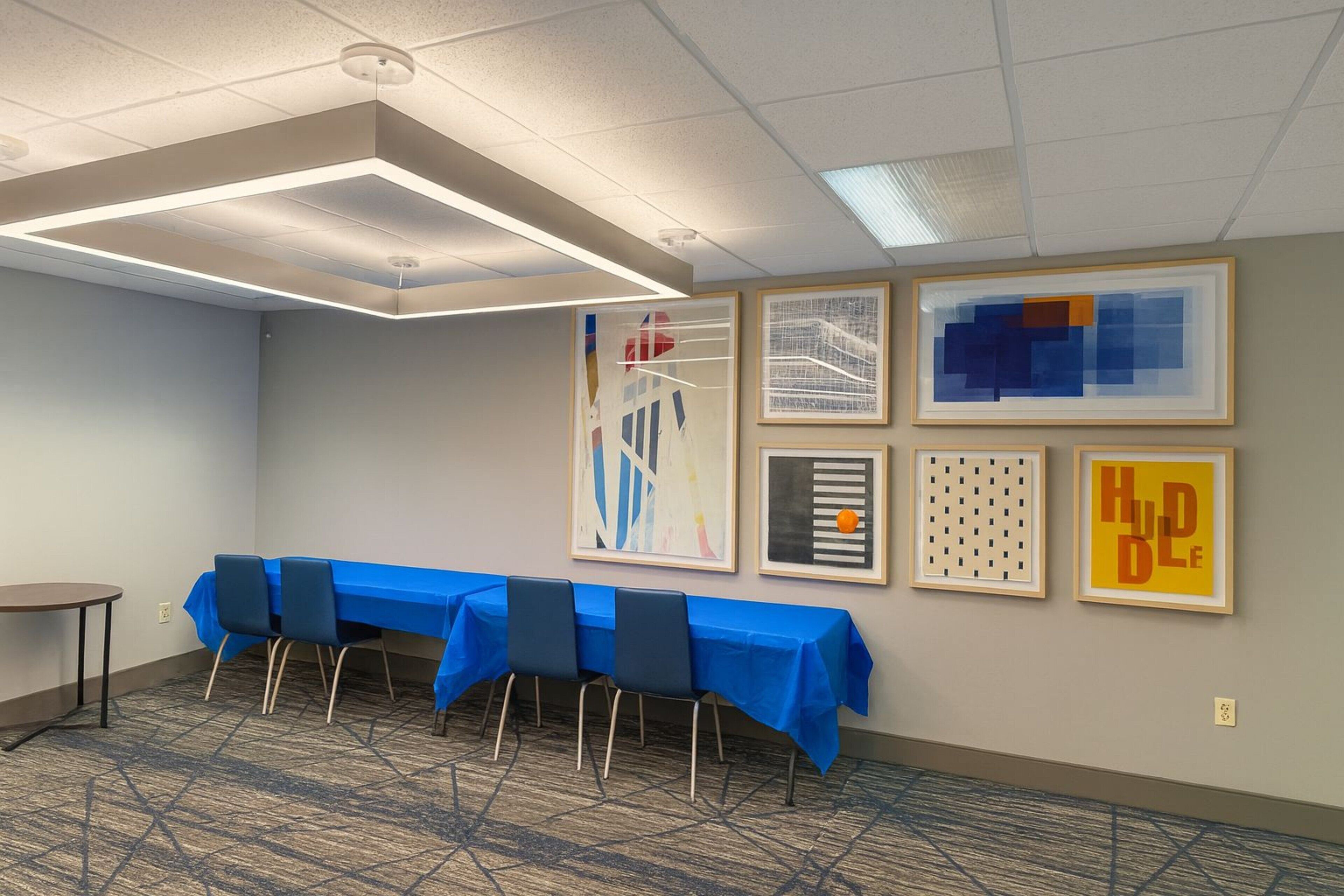 Un salón de conferencias con una larga mesa cubierta con un mantel azul, cuatro sillas y obras de arte enmarcadas en la pared.