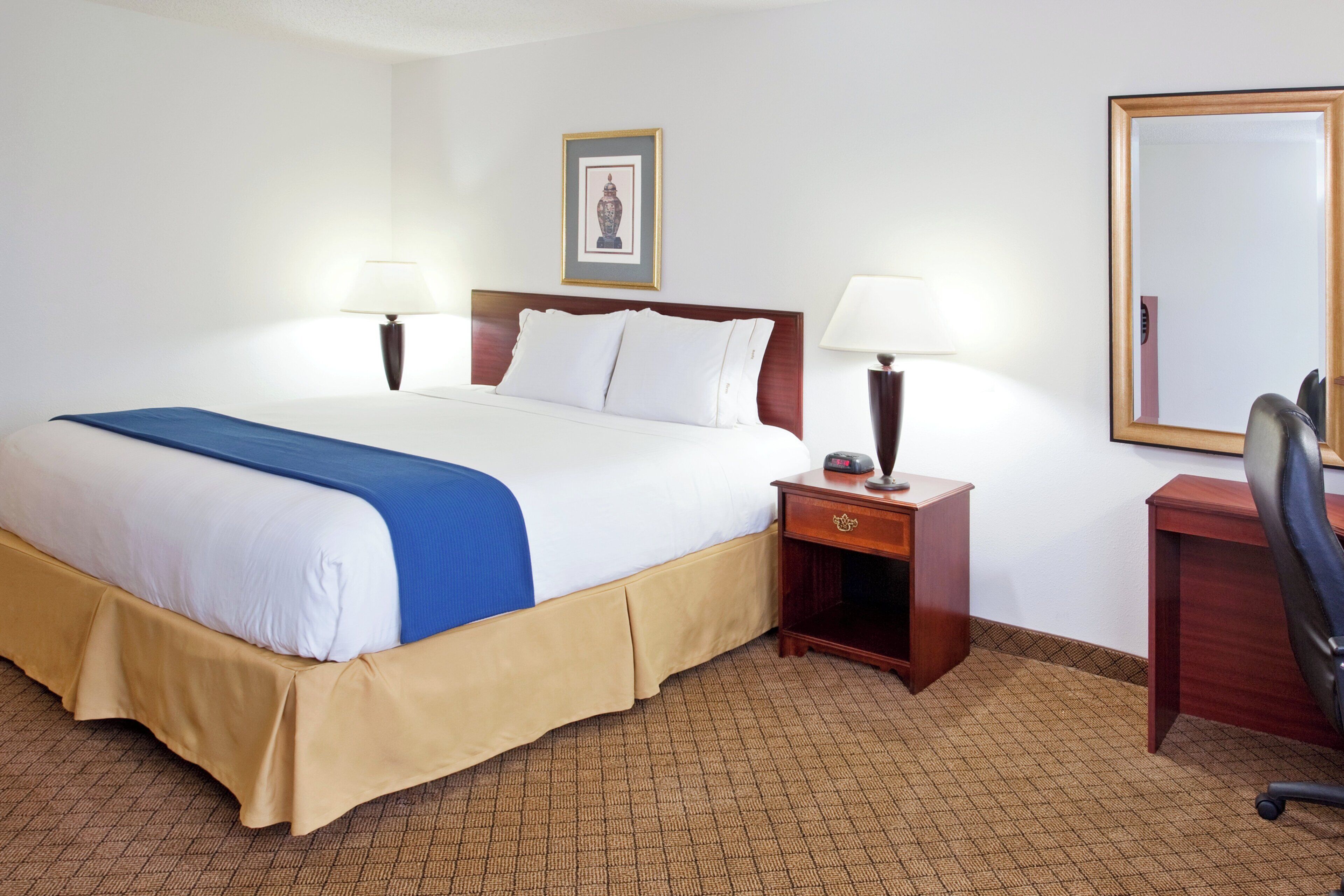 Une chambre d’hôtel comprenant un lit, des tables de chevet, un bureau, une chaise et un miroir.