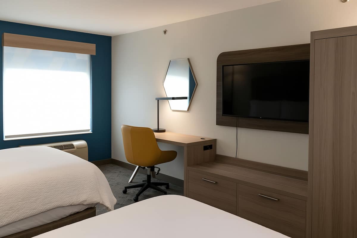 A hotel room with a bed, a desk, a chair, a TV, and a wardrobe.