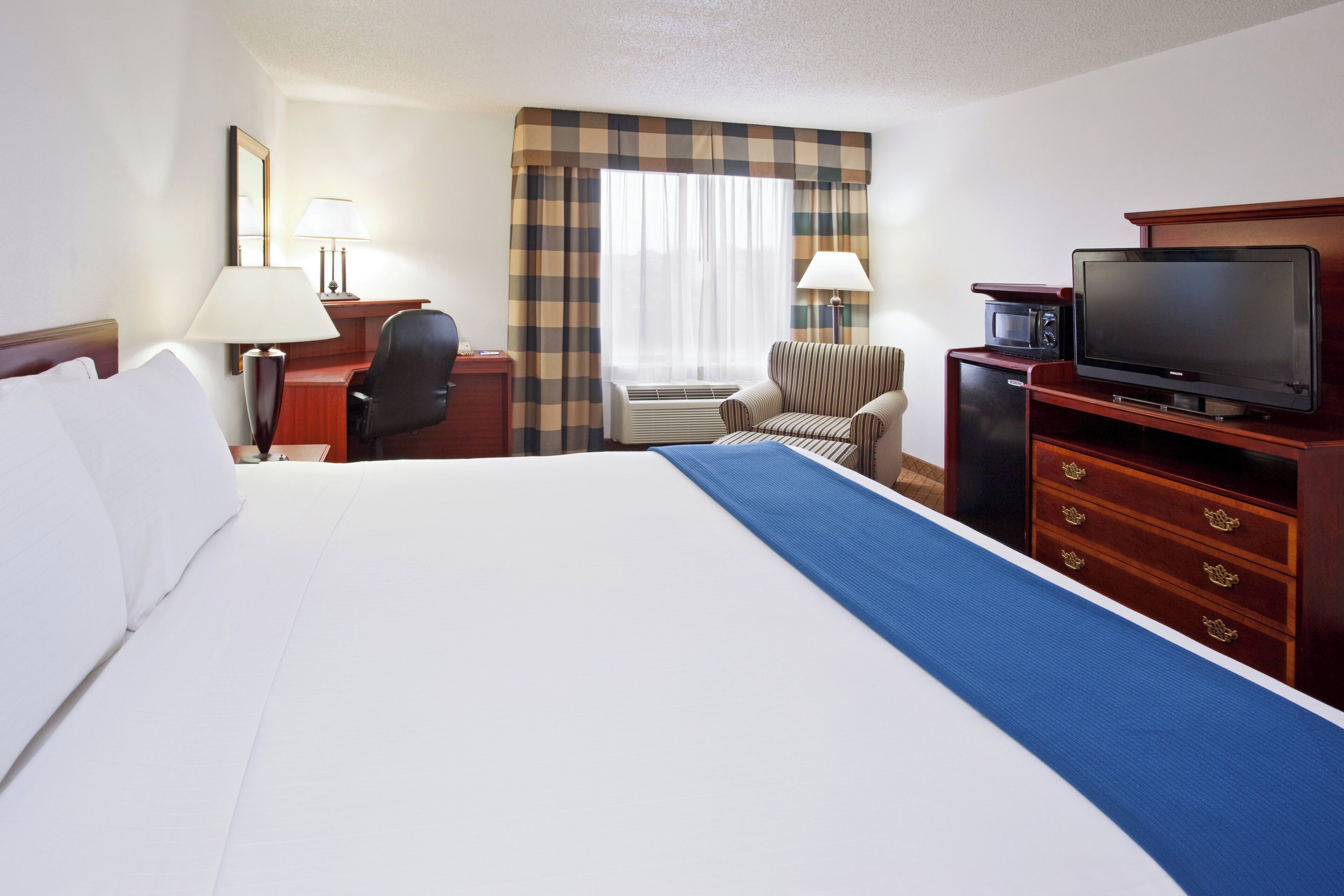 A hotel room with a large bed, a desk with a chair, a television, and a microwave.