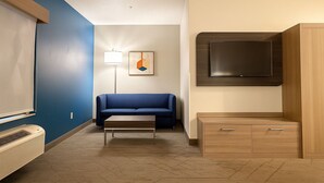 A hotel room with a blue wall, a sofa, a coffee table, a TV, and a wooden cabinet. - Holiday Inn Express & Suites Alliance by IHG (Alliance)