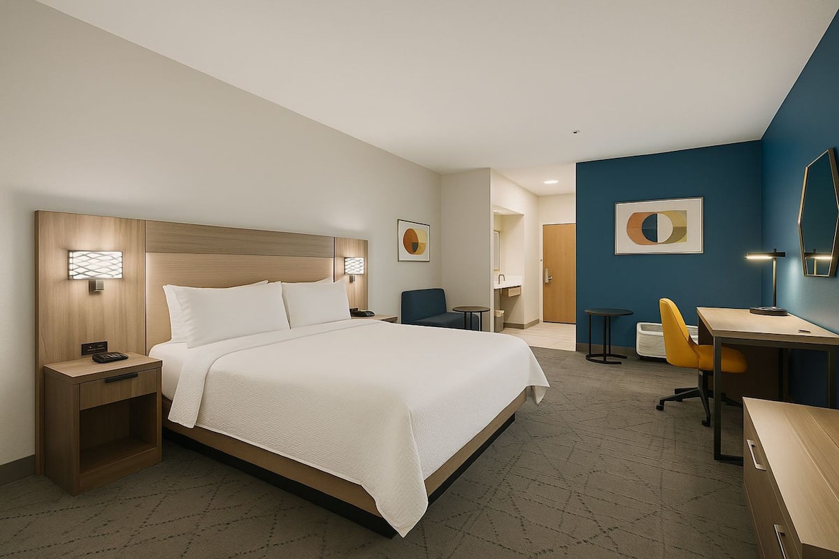 A hotel room with a large bed, a desk, a chair, and a small table.