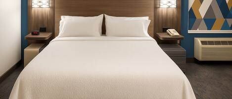 Ein Hotelzimmer mit einem großen Bett, zwei Nachttischen, einer Bank, einer wandmontierten Klimaanlage und einer Wanddekoration mit geometrischem Muster.