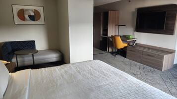 A hotel room with a bed, a sofa, a small table, a desk with a chair, a TV, and a cabinet.