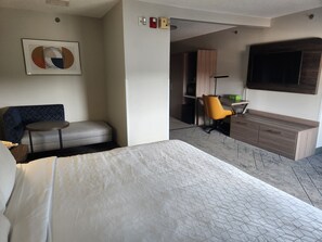 A hotel room with a bed, a sofa, a small table, a desk with a chair, a TV, and a cabinet. - Holiday Inn Express & Suites Alliance by IHG (Alliance)
