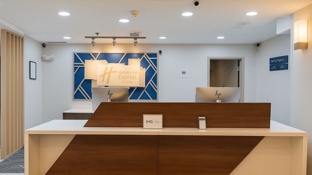A reception desk with a modern design, a blue geometric wall art piece, and a sign for 'Holiday Inn Express & Suites'. - Holiday Inn Express & Suites Alliance by IHG (Alliance)