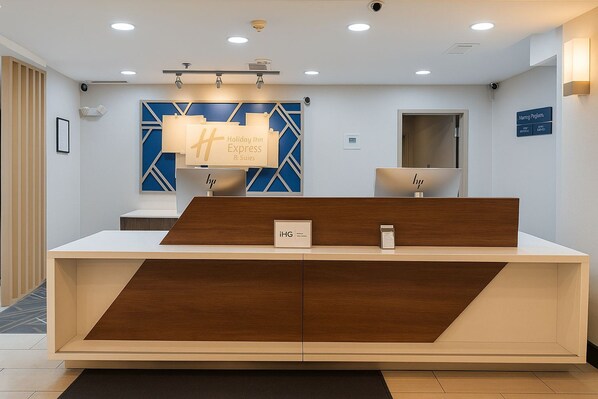 Una recepción de diseño moderno, una obra de arte geométrica azul en la pared y un letrero que dice 'Holiday Inn Express & Suites'.