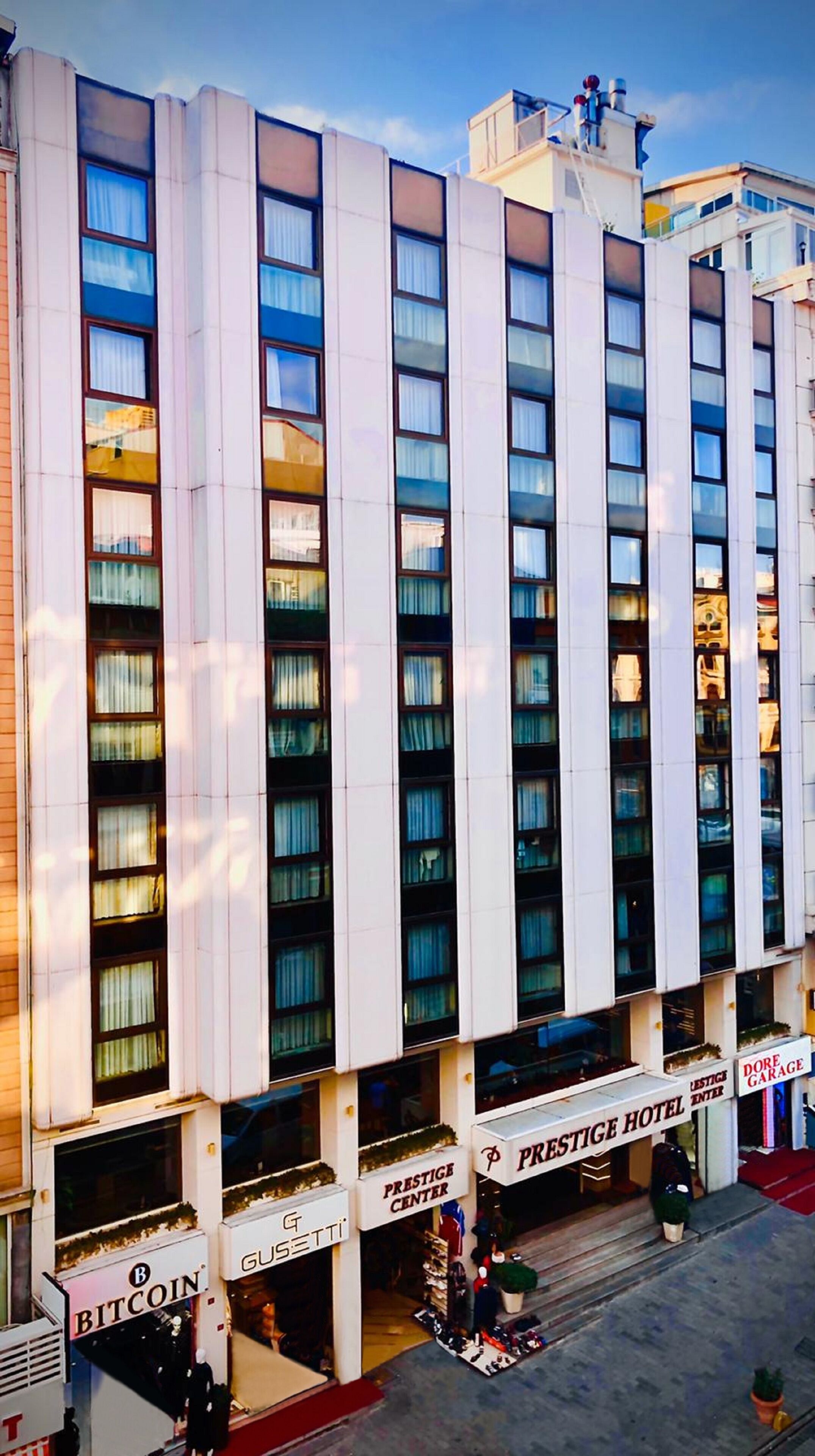 Ett hotell med flera våningar, en central entré, en väl synlig skylt med texten ”Prestige Hotel” och en skylt med texten ”Dore Garage” på höger sida.