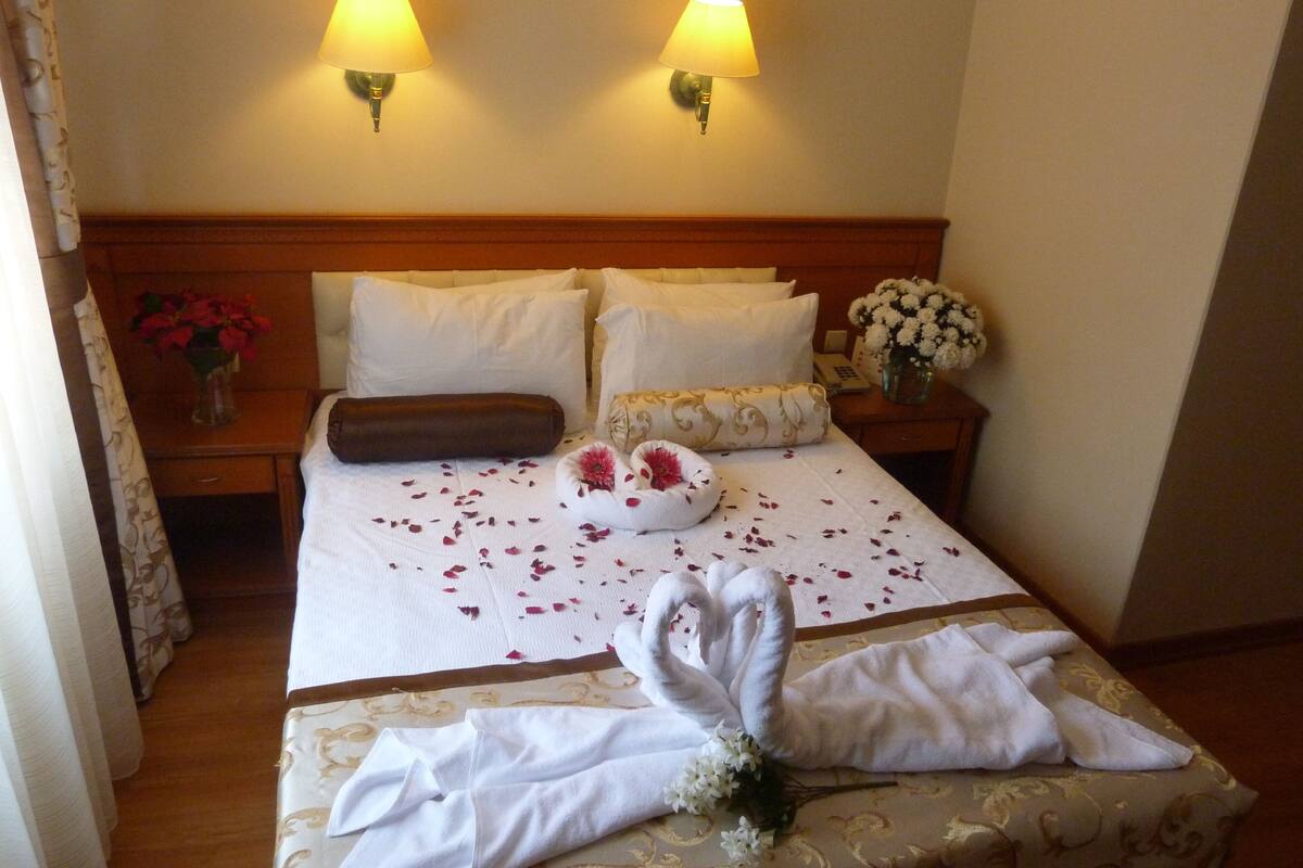 A hotel room with a neatly made bed, two bedside lamps, a vase with flowers, and a telephone on the nightstand.