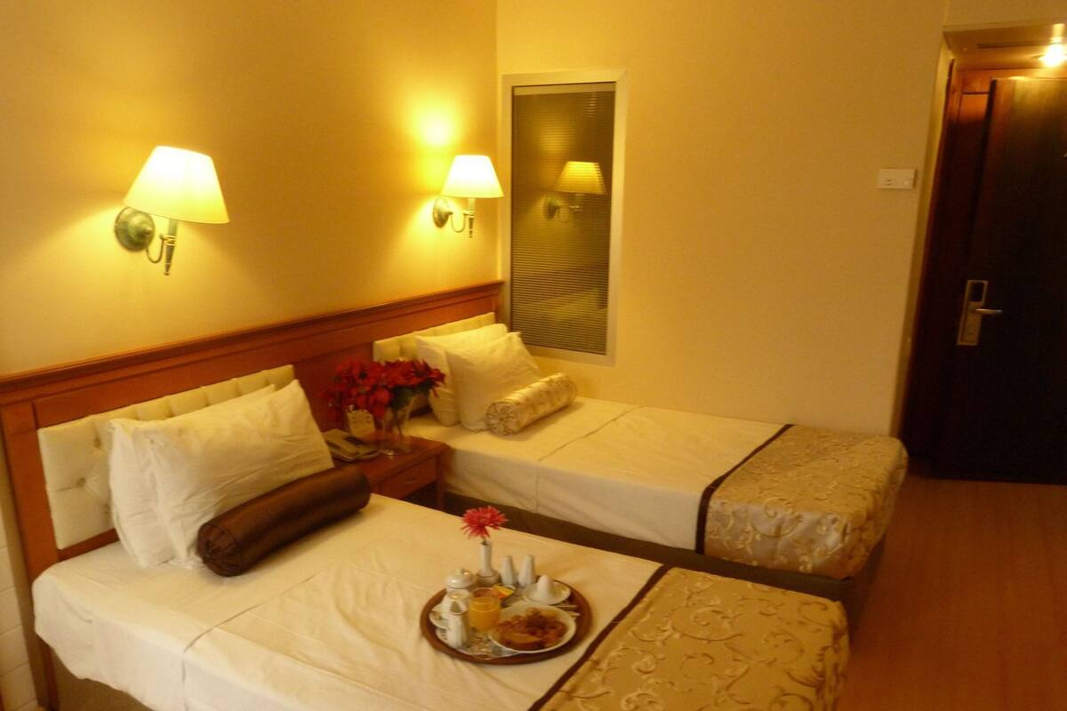 A hotel room with two beds, a nightstand with a lamp, a mirror, and a tray with breakfast items.
