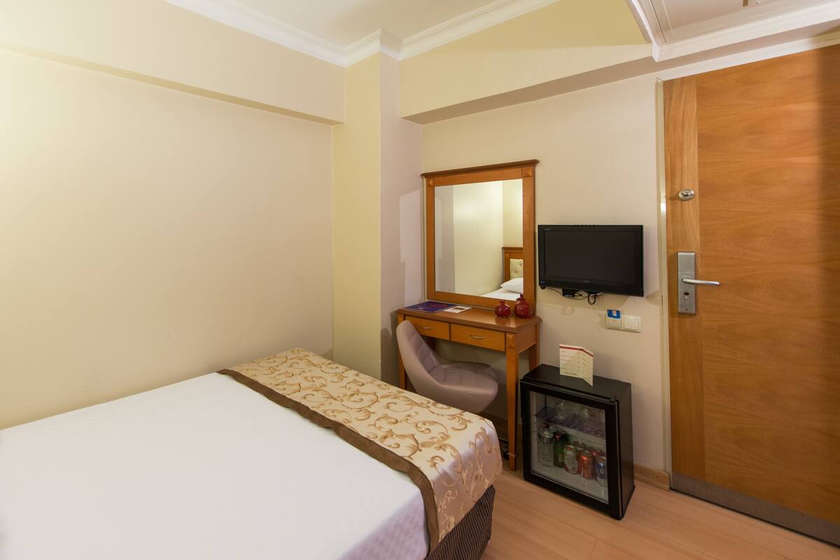 A hotel room with a bed, a desk with a chair, a television, and a minibar.