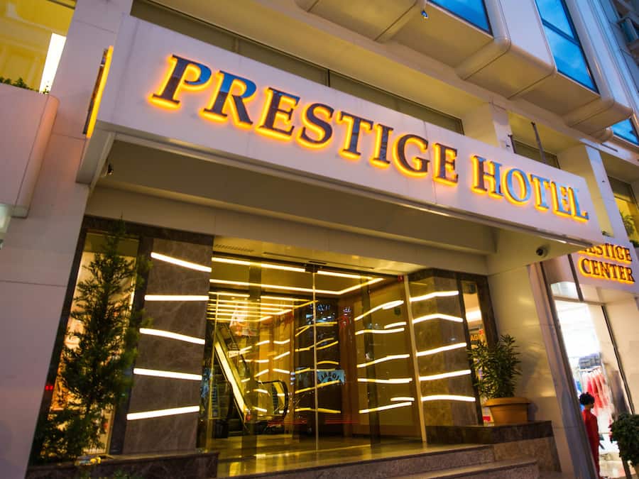 El exterior del Hotel Prestige, con un llamativo letrero iluminado, entrada de cristal y una escalera visible que lleva a la entrada.