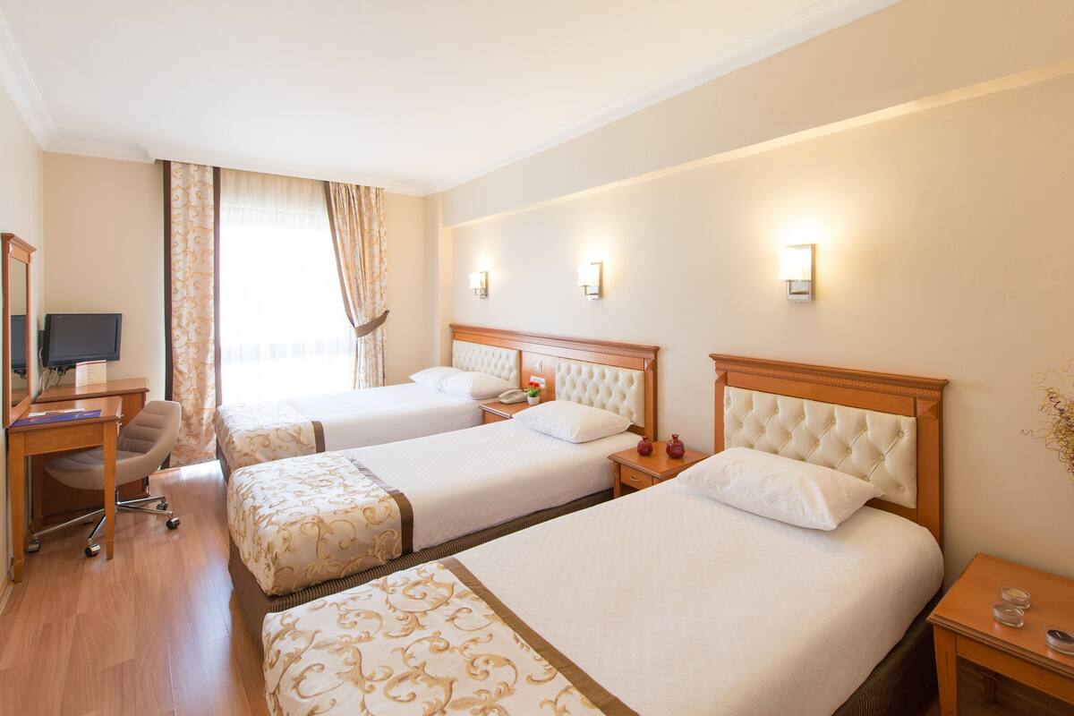 A hotel room with two beds, a desk with a chair, a TV, and a window with curtains.