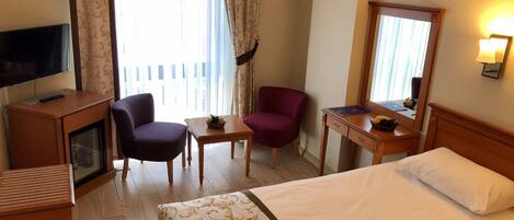 Habitación de hotel con cama, escritorio, silla, televisor y ventana con cortinas.