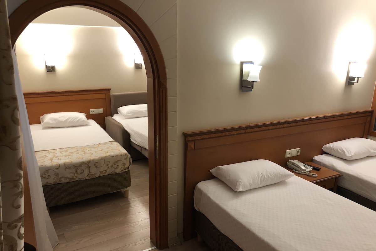 A hotel room with three beds, a wooden headboard, a telephone, and a wall-mounted light fixture.