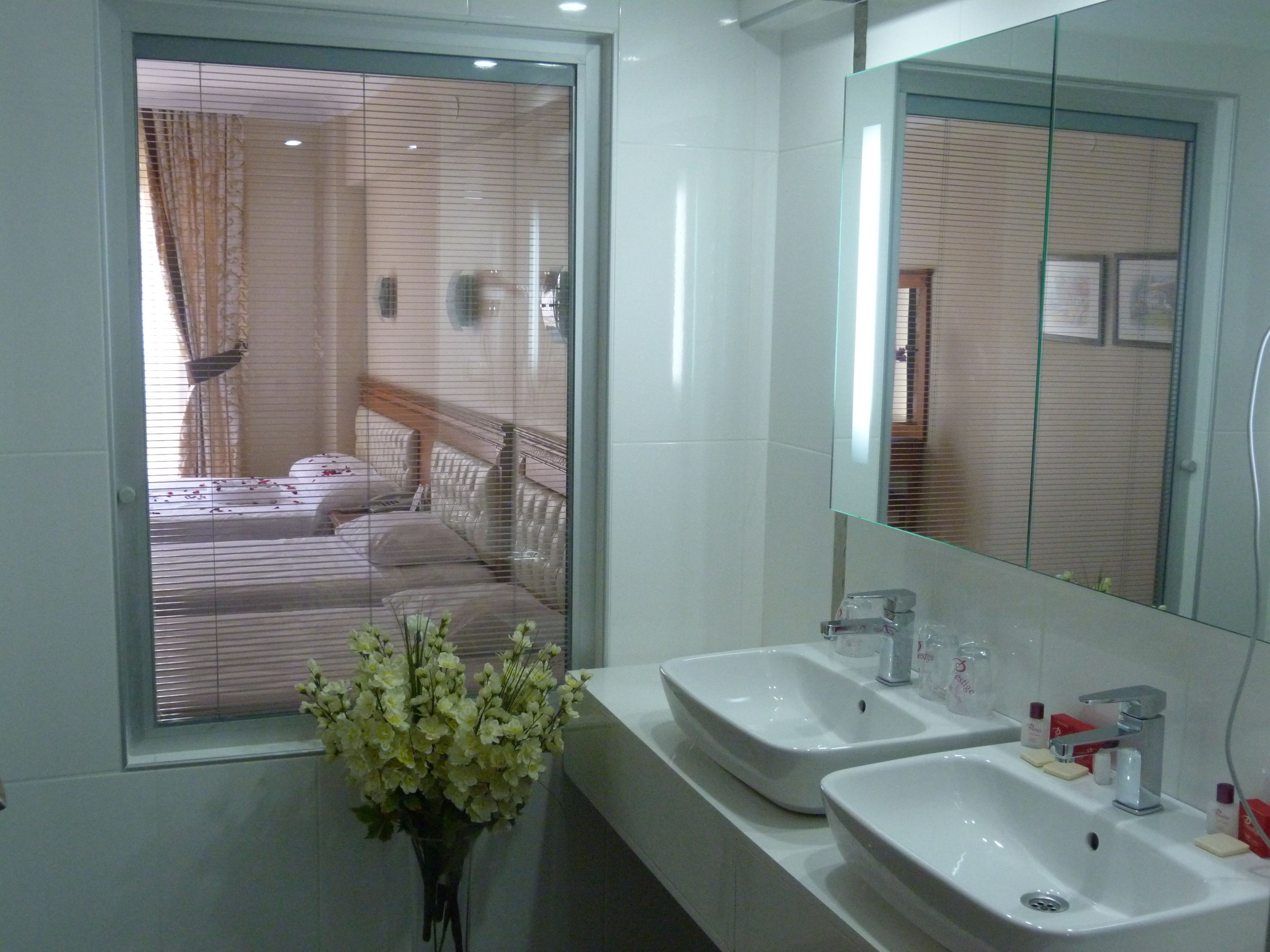 Une salle de bain moderne avec deux lavabos, un grand miroir et une fenêtre équipée de stores.