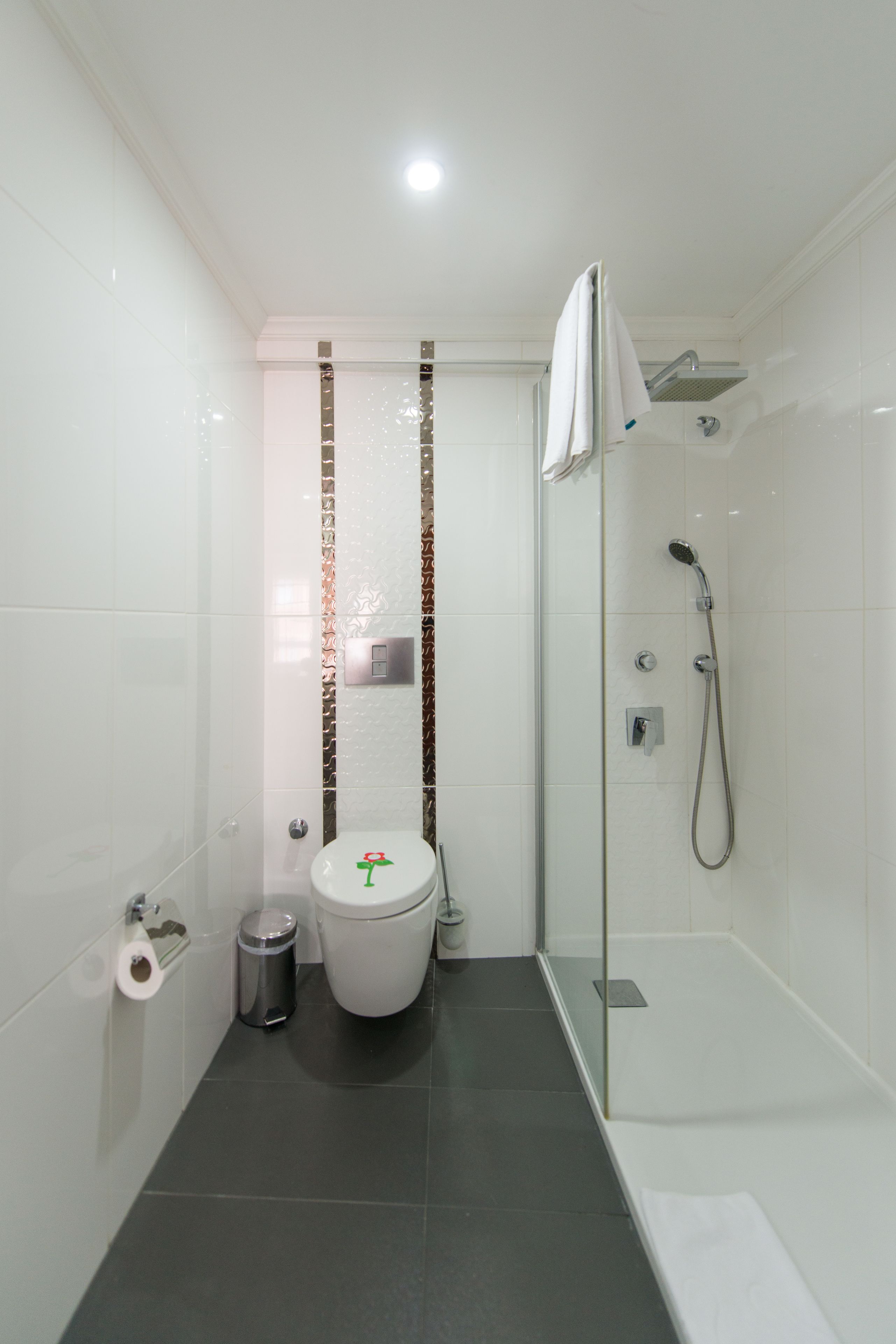 Un baño moderno con inodoro, ducha y un cubo de basura.