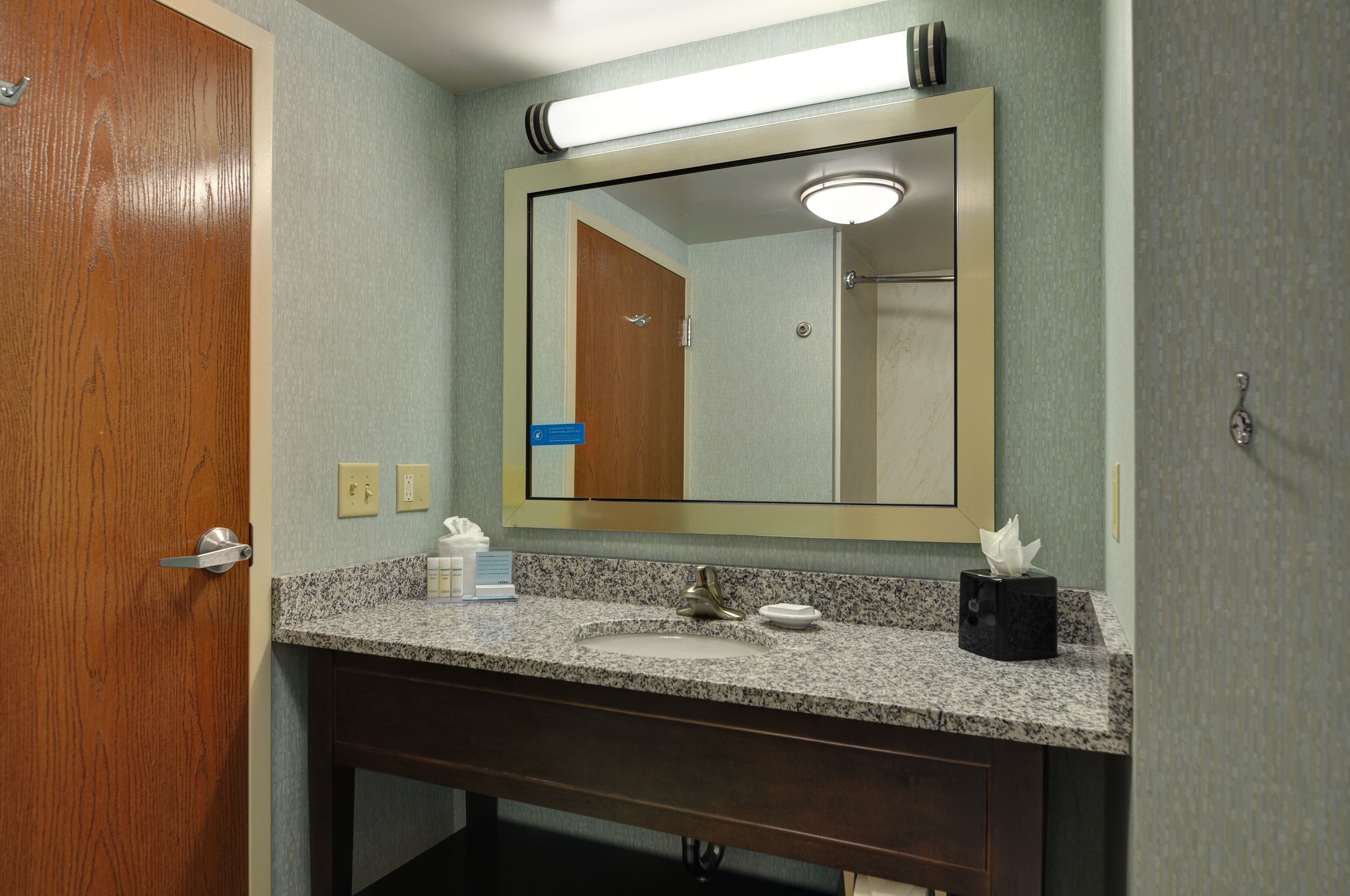 A bathroom with a granite countertop, a sink, a mirror, and a door.