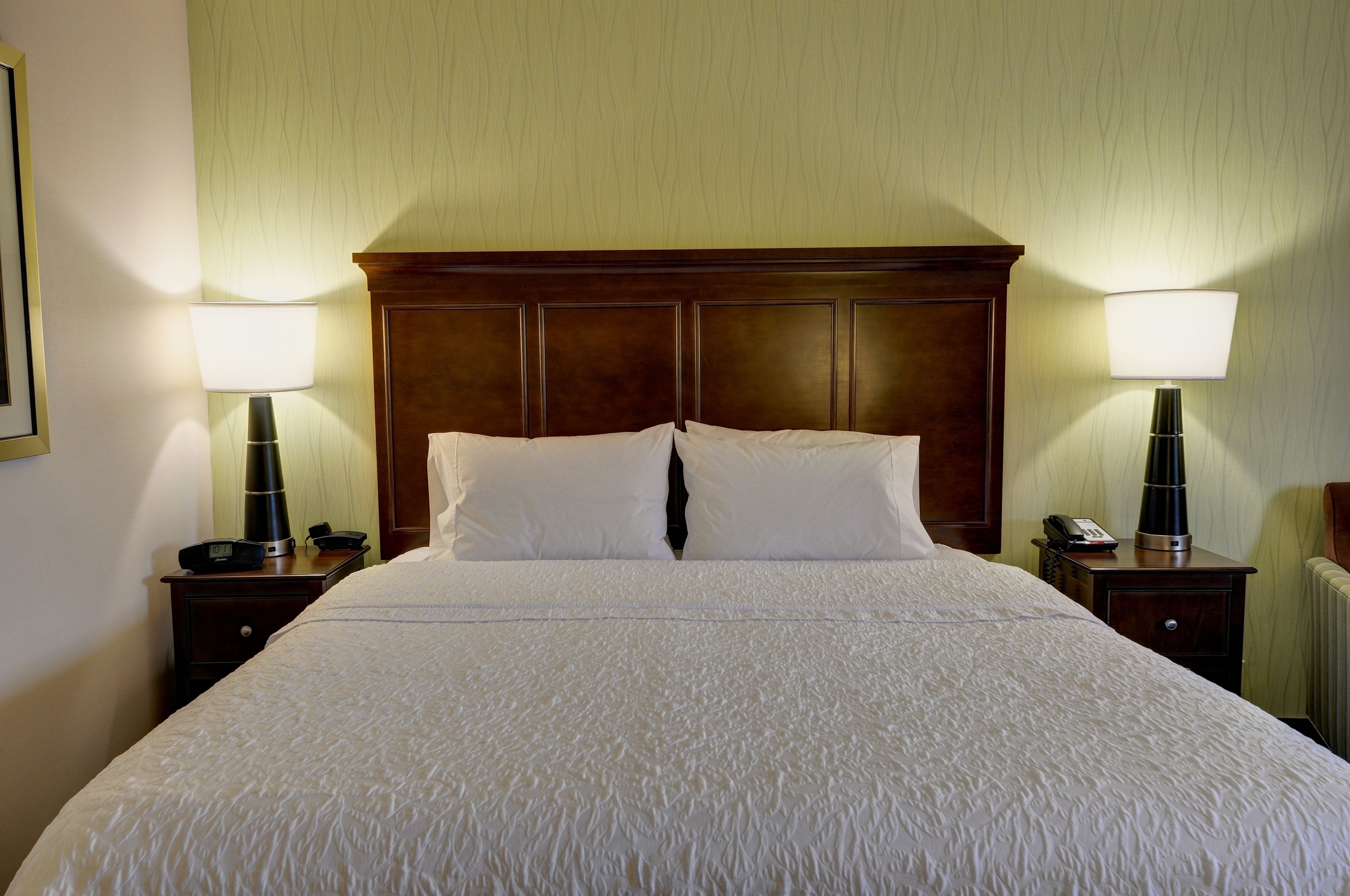 A neatly made bed with white linens, two bedside tables with lamps, and a wooden headboard.
